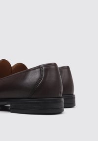 Zapatos de cuero marrón con un diseño elegante, tacones redondeados y una suela negra texturizada. Costuras detalladas a lo largo de los bordes.