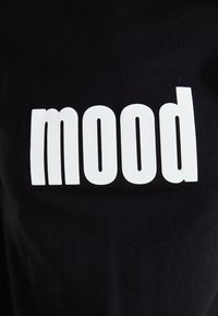 Crna pamučna majica s natpisom "mood" u velikom bijelom podebljanom fontu. Tekst ima glatku površinu koja se lijepo uklapa u meku teksturu tkanine.