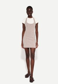 Gestreepte minidress met een vierkante halslijn, mouwloos ontwerp en zijknopen. Draag het over een witte, aansluitende blouse. Bruine klompen als schoeisel.