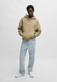 Beige hoodie met logo, gecombineerd met lichtblauwe geblokte jeans en witte sneakers. Eenvoudig ontwerp, relaxte pasvorm, ongecompliceerde texturen.