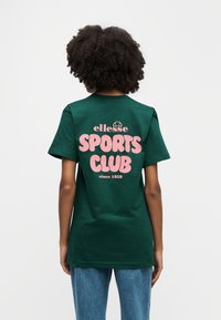 Πράσινο βαμβακερό t-shirt με ροζ κείμενο που αναγράφει "SPORTS CLUB" και "ellesse since 1959" στην πλάτη, κοντά μανίκια, κλασική γραμμή.