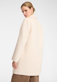 Cappotto in lana crema con colletto sagomato, spalle scese, tasche laterali e silhouette dritta. Texture morbida, design minimale.
