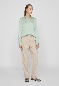 Light green satin blouse with a collar, beige straight-leg trousers, and patterned black and beige shoes. Simple and sleek design.