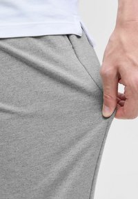Szare, teksturowane szorty sportowe z dopasowaną talią, pokazane lekko naciągnięte, ukazujące elastyczny materiał i luźny krój.