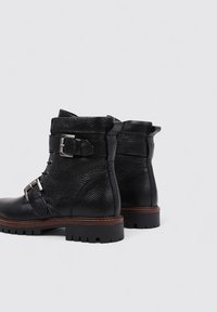 Bottines en cuir noir avec une finition texturée, présentant des accents en métal argenté, une boucle sur le côté et une semelle robuste.