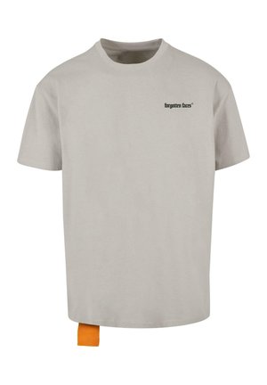 T-shirt en coton gris clair avec des manches courtes, arborant un petit logo noir sur la poitrine gauche et une étiquette orange en bas à gauche.