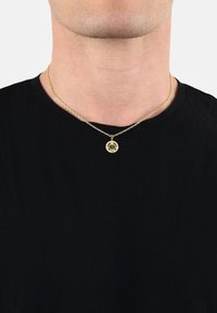 Man som bär ett guldhalsband med en rund pendant som har en krabba och siffran 69, över en svart crewneck-tröja.