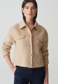 Beige wollen blend jas met een kraag, knoopsluiting en twee borstzakken. Met een cropped ontwerp en opgerolde mouwen.