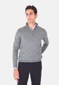 Maglione grigio con zip in un morbido tessuto a maglia, con colletto alto e polsini a costine, abbinato a pantaloni blu navy.