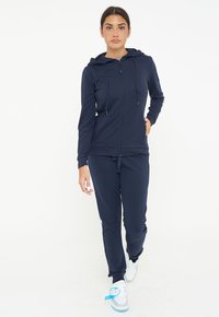 Felpa con zip di colore navy e pantaloni coordinati, realizzati in tessuto morbido, con cappuccio regolabile, vestibilità slim e polsini alle caviglie.