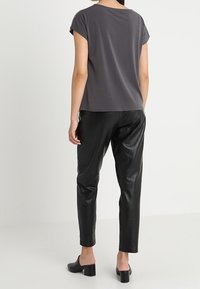 Šedý top s krátkým rukávem v kombinaci s černými kalhotami z umělé kůže. Oblečení má volný střih a jemný lesk na látce. Černé muly na blokovém podpatku.