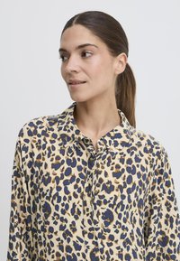 Leopardenmuster-Hemd mit einem cremigen Grundton und blauen sowie braunen Flecken, klassischem Kragen, durchgehender Knopfleiste und weichem Stoffgefühl.