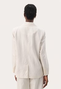 Blazer blanco de rayas con un corte entallado, abertura simple y un brillo sutil. Presenta solapa muesca y puños de tres botones.