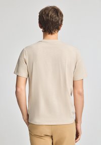 T-shirt beige a maniche corte in tessuto morbido e testurizzato. Presenta un colletto rotondo e una vestibilità rilassata, con cuciture visibili lungo i bordi.