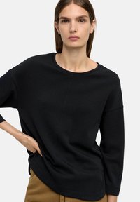 Czarna, długosleeve'owa bluzka z okrągłym dekoltem i luźnym krojem, wykonana z miękkiego materiału, z widocznymi szwami i delikatną teksturą.