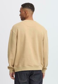 Beige cotton sweatshirt with a relaxed fit, ribbed cuffs, and a round neckline. Smooth texture, no visible patterns or logos.