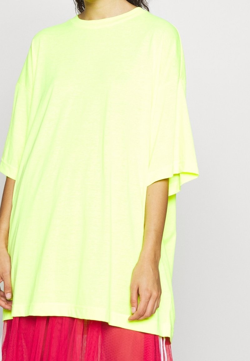 T-shirt oversize gialla neon in tessuto leggero con scollo rotondo e maniche corte, caratterizzato da una vestibilità ampia e rilassata.