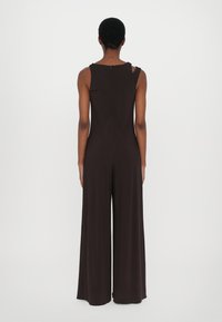 Brun, ärmlös jumpsuit med vida ben, slät textur, bakdragkedja och axelutsnitt. Minimalistisk design, enfärgad.