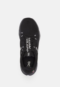 Schwarzer Sportschuh mit einem atmungsaktiven Mesh-Obermaterial, kontrastierenden weißen Logos, flachen Schnürsenkeln und einer abgerundeten Zehenpartie. Texturierte Sohle mit leichter Krümmung.