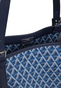 Sac fourre-tout texturé de couleur bleue, en matériau synthétique, avec un design géométrique dans des teintes plus claires. Inclus une étiquette à l'intérieur.