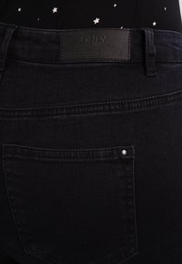 Jeans de mezclilla negros con un bolsillo trasero con un remache de metal, una etiqueta de cuero en la cinturilla y detalles de costura sutiles.
