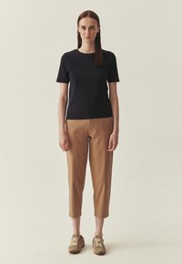 T-shirt noir à manches courtes et cintré, associé à un pantalon raccourci de couleur beige. La tenue est complétée par des baskets lacées marron clair.