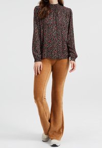 Svart blommig blus med hög krage och långa ärmar, kombinerad med tan ribbade utsvängda byxor. Båda plagg har en texturerad yta.