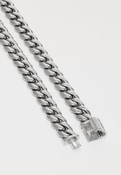 Close-up of a silver curb chain necklace with interlocking links and a clasp open on one end.