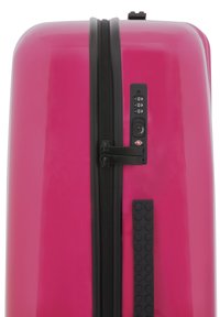 Hard-shell suitcase in glossy pink with black zipper, combination lock, and textured grip accents on the side.