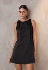 Mustaton olkaimeton mekko, jossa on nauha-yksityiskohtia olkapäillä, ja se on varustettu istuvalla vartalonmyötäisellä yläosalla ja laajahelmaisella hameella. Silkkinen kangas, jossa on mattapinta.