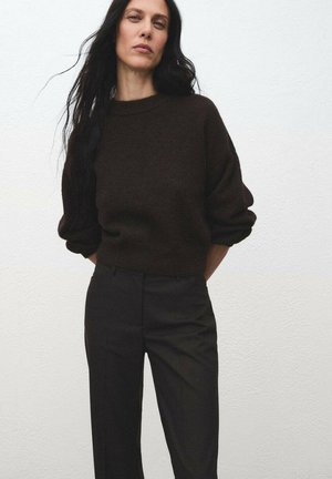 Suéter de punto marrón con cuello redondo y hombros caídos, combinado con pantalones negros de talle alto en una tela texturizada.