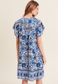 Kurzärmliges Kleid mit einem blauen und schwarzen Blumenmuster auf weißem Hintergrund, rüschensäumigen Ärmeln und einem mittellangen Saum.