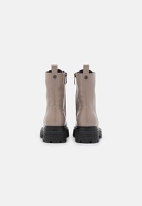 Stivaletti alla caviglia in pelle beige con finitura liscia, suola in gomma nera, cerniera sul retro e bottoni decorativi alla caviglia.