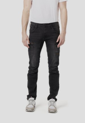Pantalones cargo de mezclilla negra con múltiples bolsillos, corte ajustado y detalles sutiles de costura. Combinados con zapatillas grises y blancas.