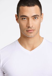 Biała koszulka V-neck wykonana z gładkiego, lekkiego materiału, dopasowana do ciała z prostymi liniami i minimalnymi detalami.