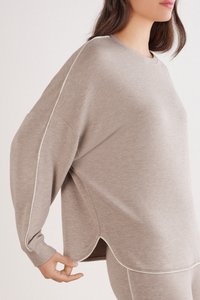 Beige oversized sweatshirt met lange mouwen, een gebogen zoom en contrasterende witte stiknaden. Gemaakt van een zachte, gestructureerde stof.