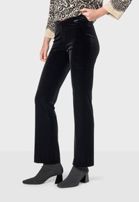 Čierne zamatové rozšírené nohavice s hladkou textúrou, s bočnými švami a priliehavým pásom, v kombinácii so šedými členkovými čižmami.