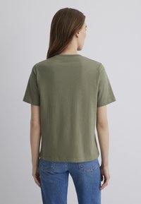 Olive green cotton t-shirt with short sleeves, round neckline, and a relaxed fit. Fabric appears soft with a smooth texture.