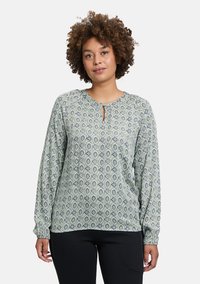 Langärmlige Bluse in hellem Grün mit einem umfassenden Blattmuster in Marineblau und Weiß, ausgestattet mit einem Schlüsselloch-Ausschnitt und elastischen Manschetten.