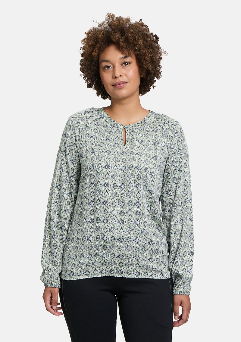 Langärmlige Bluse in hellem Grün mit einem umfassenden Blattmuster in Marineblau und Weiß, ausgestattet mit einem Schlüsselloch-Ausschnitt und elastischen Manschetten.
