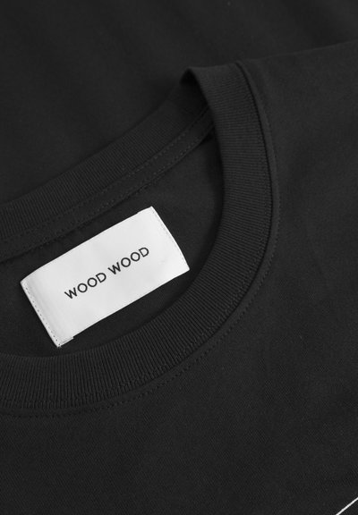 Tricou din bumbac negru cu guler rotund și guler tricotat plat. Prezentă un etichetă albă cu "WOOD WOOD" imprimat în negru.