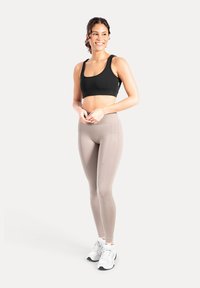 Sort sports-bh og beige leggings lavet af strækbart materiale, med en glat tekstur og minimalistisk design, kombineret med hvide sportssko.