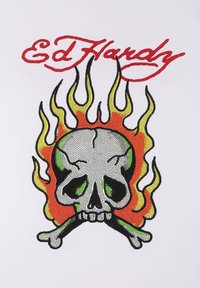 Tričko Ed Hardy s šedou lebkou se zelenými akcenty, zkříženými kostmi a plamennými vzory v oranžové a žluté barvě, vše na bílém pozadí.