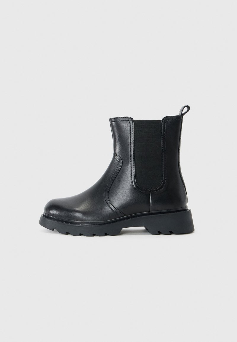 Botte de cheville en cuir noir avec des panneaux élastiques sur les côtés, bout rond et semelle en caoutchouc texturé. Dispose d'une languette à l'arrière pour un enfilage facile.