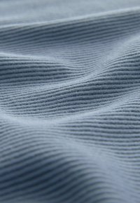 Tissu côtelé bleu clair avec une texture douce, présentant des motifs ondulés subtils et des variations de teinte à travers la surface.