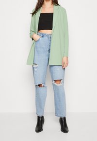 Ljusgrön kavaj i mjukt material, svart crop top, slitna ljusblå jeans och svarta ankelboots, med lös passform och revor.