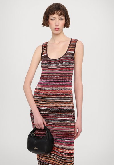 Strapless, form-fitting dress with a wavy striped pattern in various colors. Model holds a small black handbag with a gold logo.