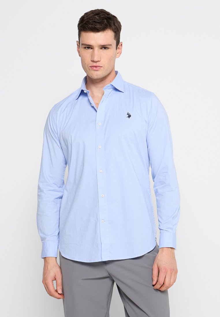 Camicia azzurra chiara a maniche lunghe con colletto a punta, chiusura frontale con bottoni e un piccolo logo nero sul lato sinistro del petto. Vestibilità standard.