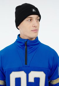 Blauwe sportjack met ritskraag en mesh stof, voorzien van opvallende witte cijfers en accentstrepen. Zwarte gebreide beanie met logo.