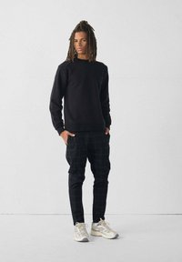 Sweatshirt noir à col ras du cou associé à un pantalon à carreaux noir. Le mannequin porte des baskets claires avec des accents réfléchissants. Design simple et décontracté.